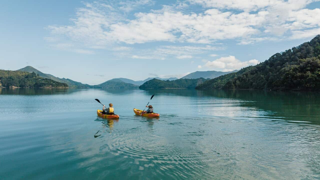 Two people canoeing side by side on remote lake with hill surrounds