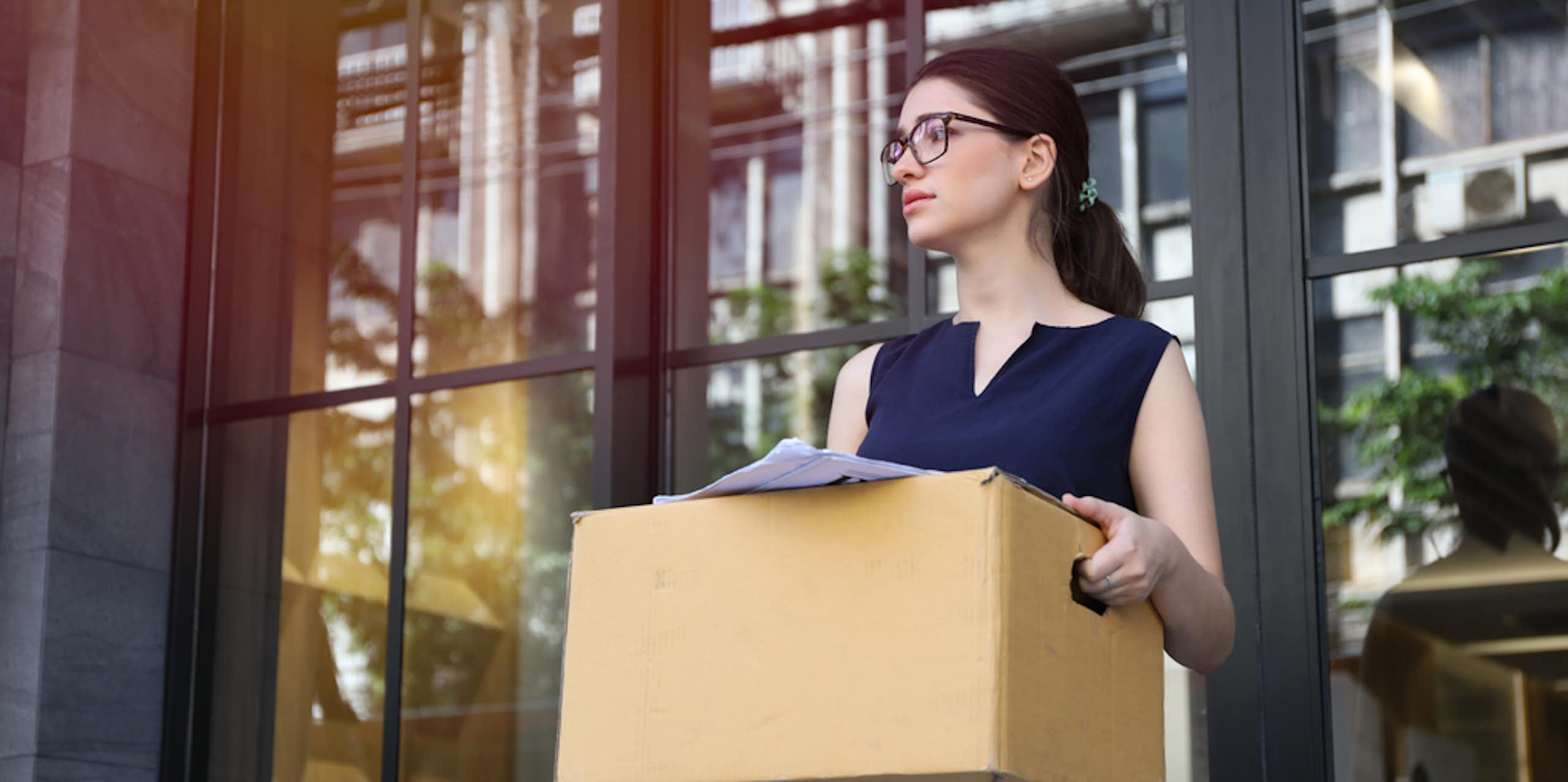 Une femme avec un carton sortant d'un bâtiment