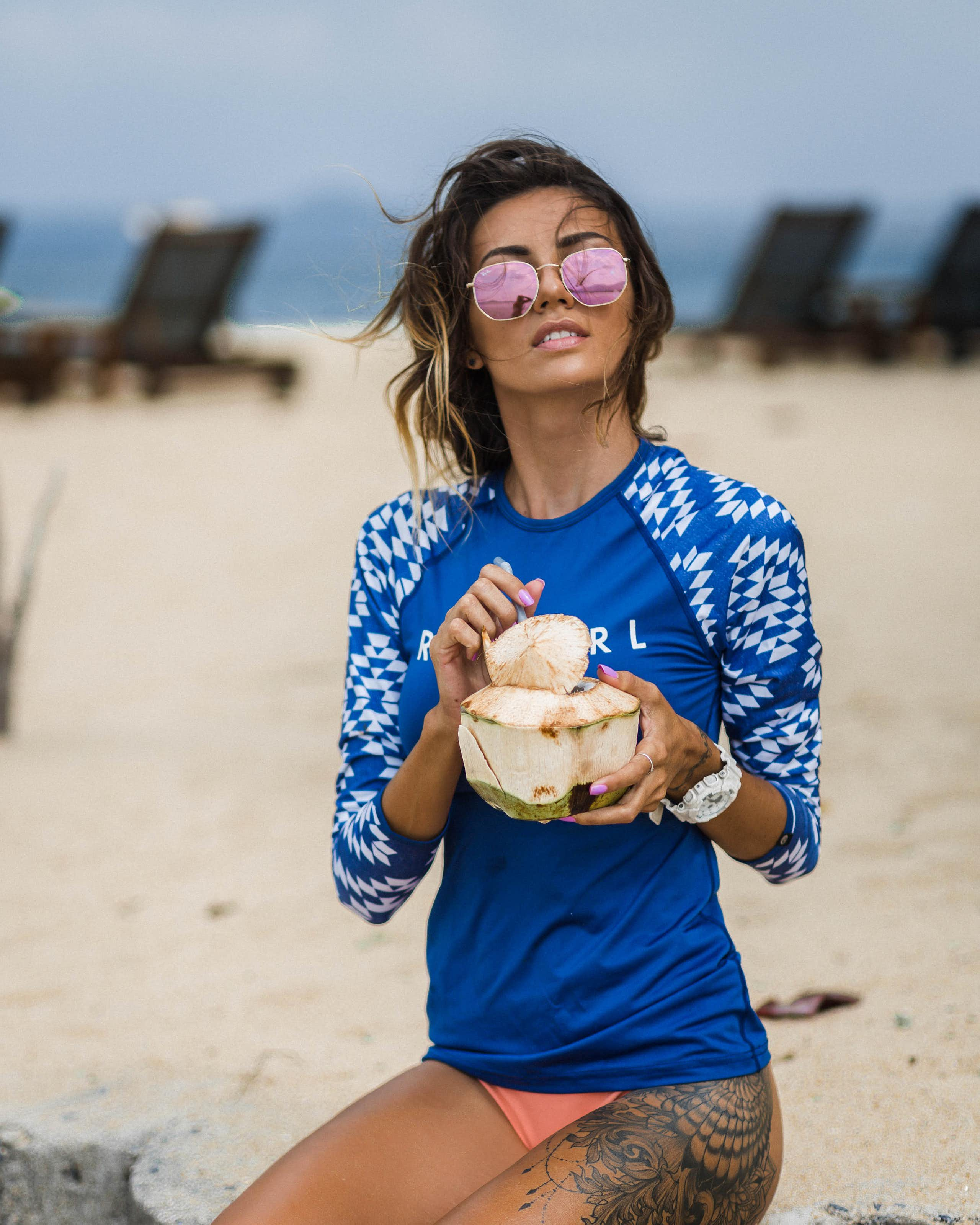 Une femme sur la plage se protège du soleil avec un vêtement conçu à cet effet et des lunettes de soleil.