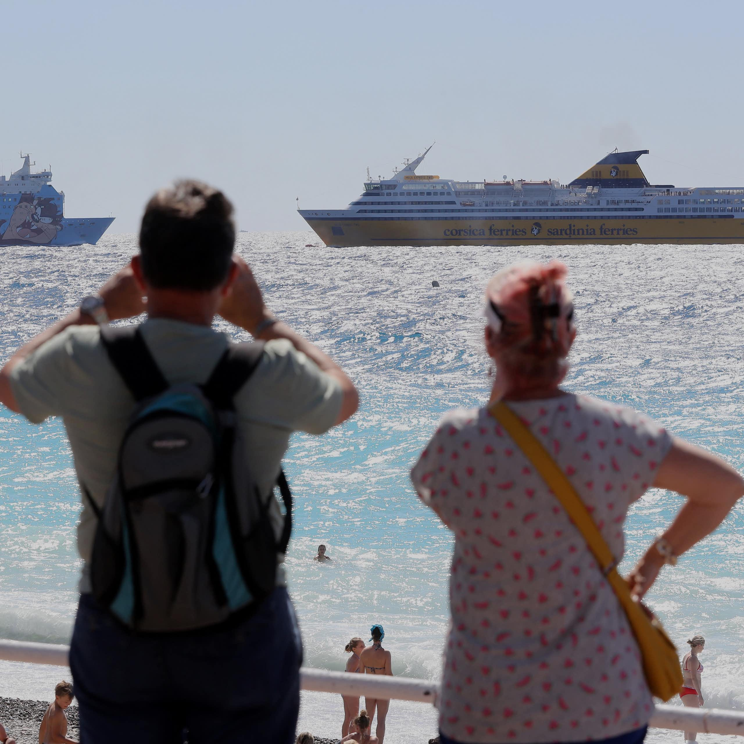 deux personnes de dos regardent des ferrys dans la mer