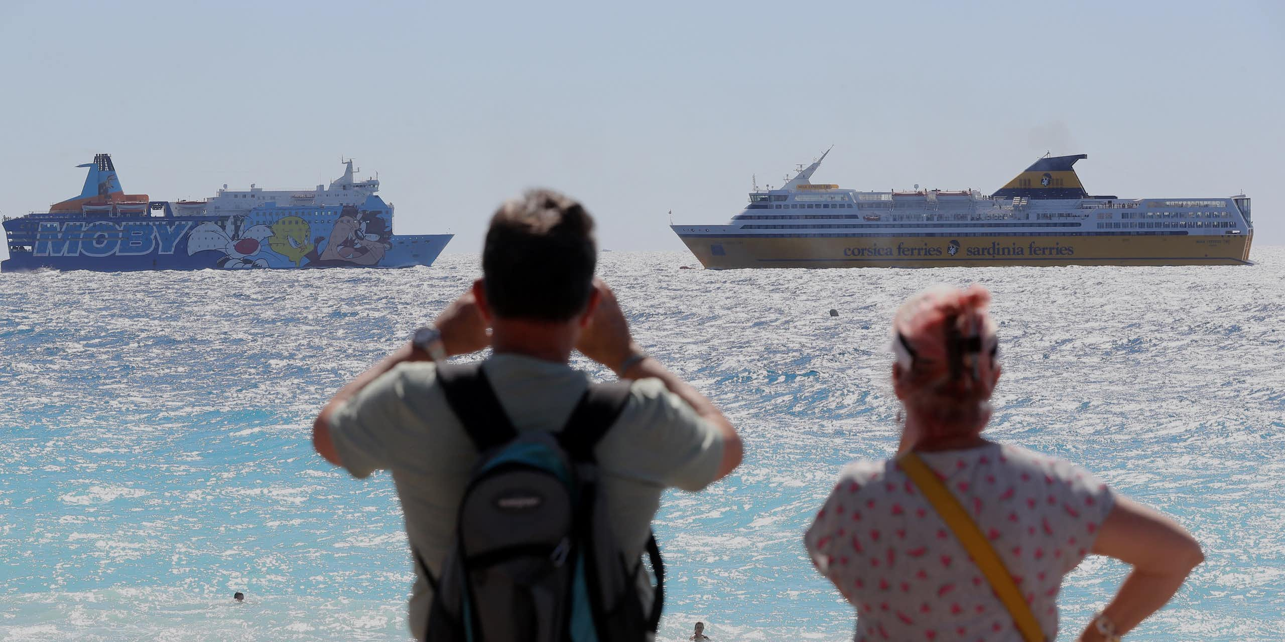 deux personnes de dos regardent des ferrys dans la mer