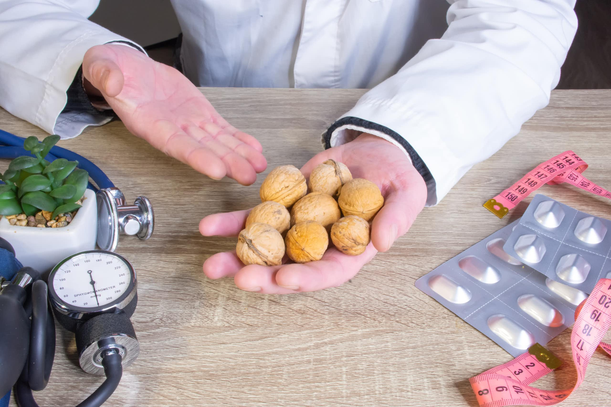 Un médecin tient dans ses mains des noix. A côté de lui, un mètre de couture et un stéthoscope.