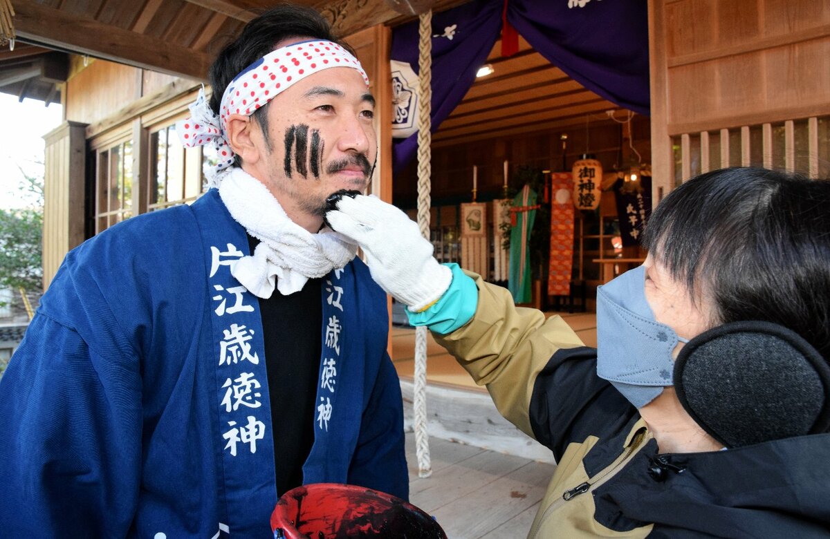 顔に墨を塗られる男性（左）＝１２日、松江市美保関町片江の方結神社