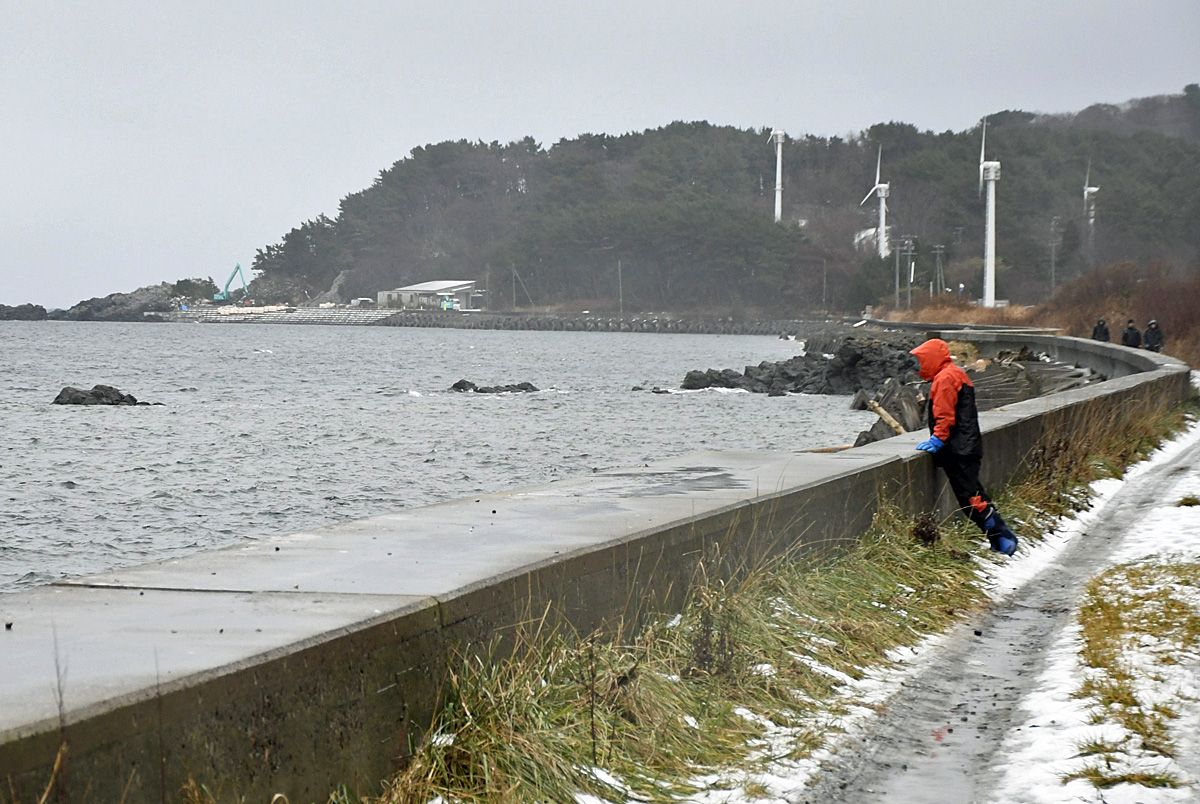 海岸線を歩きながらくまなく捜索する地元漁師たち＝21日午前8時10分ごろ、大間町大間