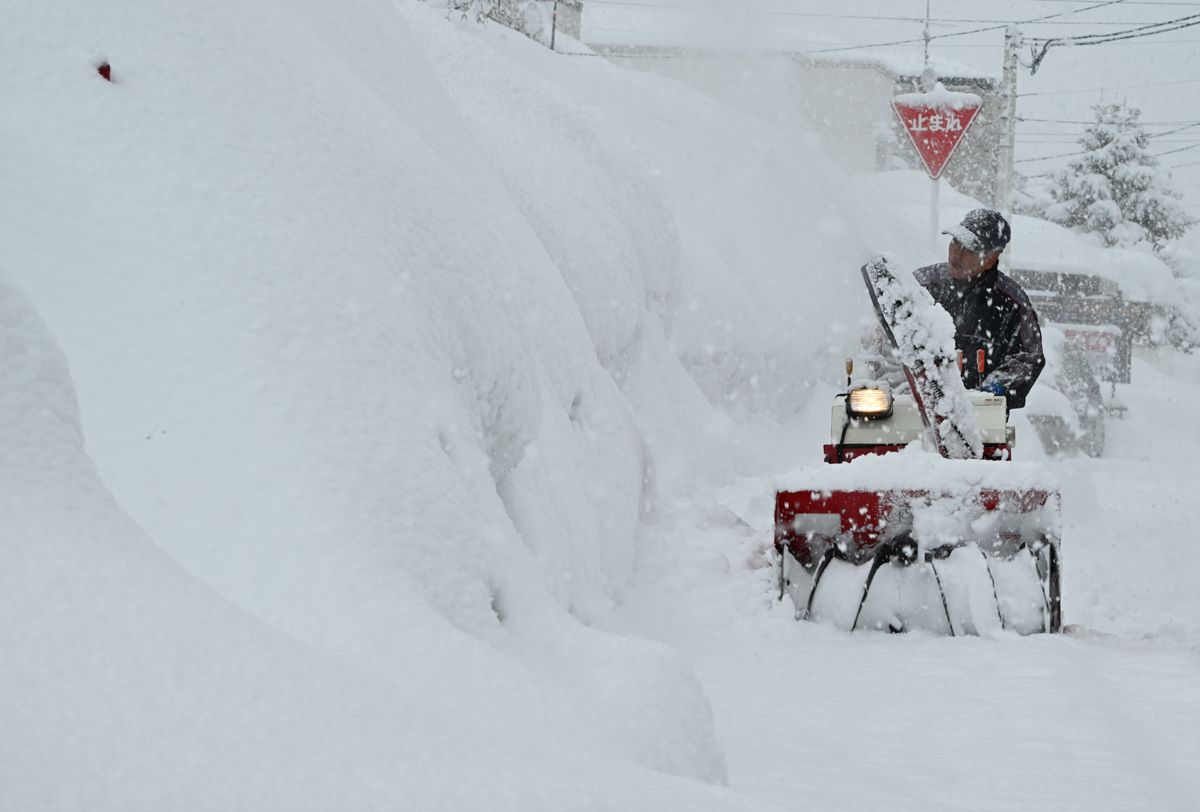 自宅前の道路にどっさり積もった雪を除雪機で飛ばす市民＝10日午前9時43分、青森市浜田1丁目