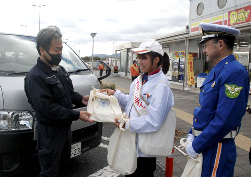 【立ち寄ったドライバーに交通事故防止を呼びかけるハイウェイレディ三重（中央）と伊藤隊長（右）＝亀山市布気町の亀山ＰＡで】