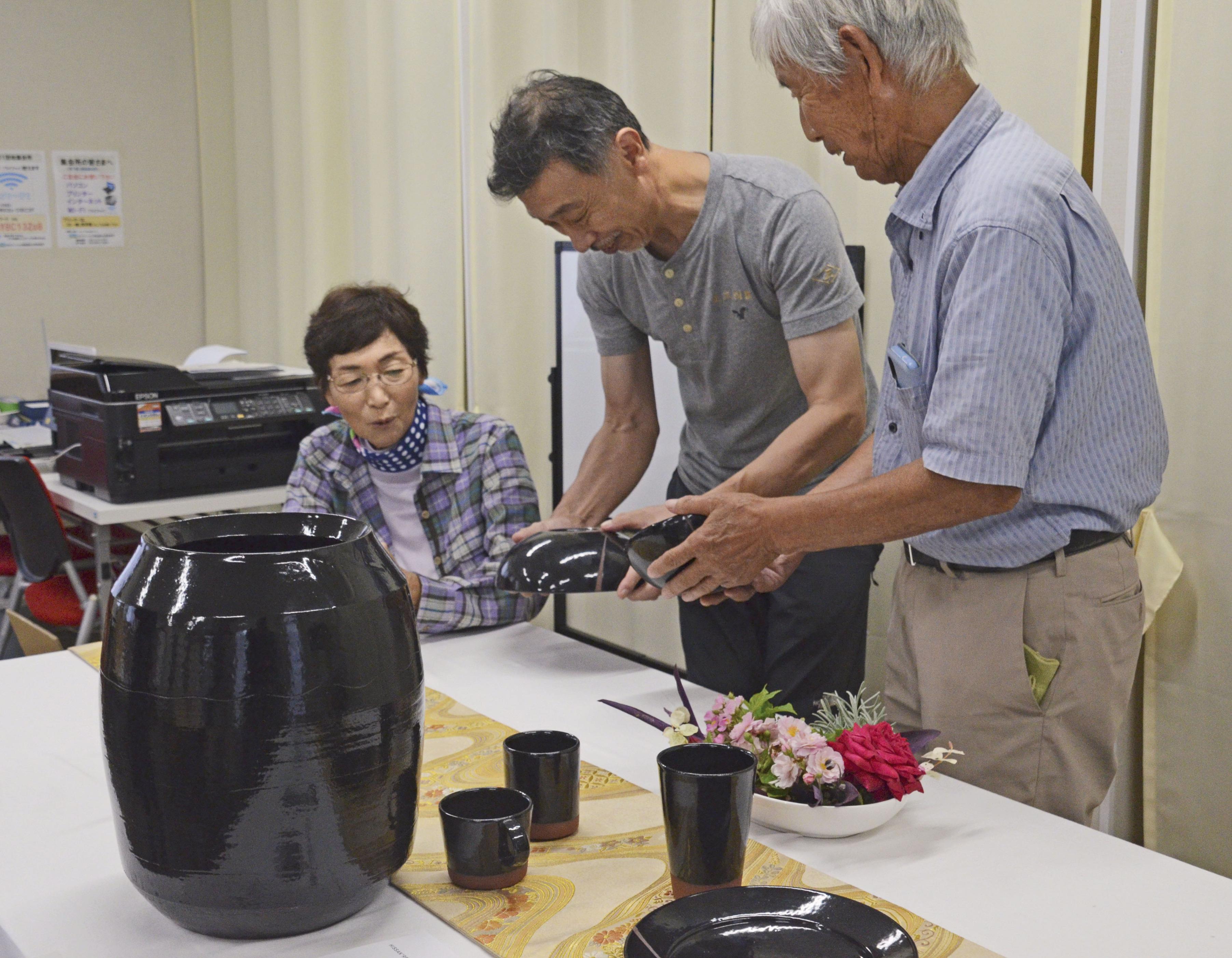 能登の瓦を材料とした信楽焼の花瓶や食器などを見る（左から）大倉好子さん、小川公男さんら＝2024年10月、石川県輪島市門前町