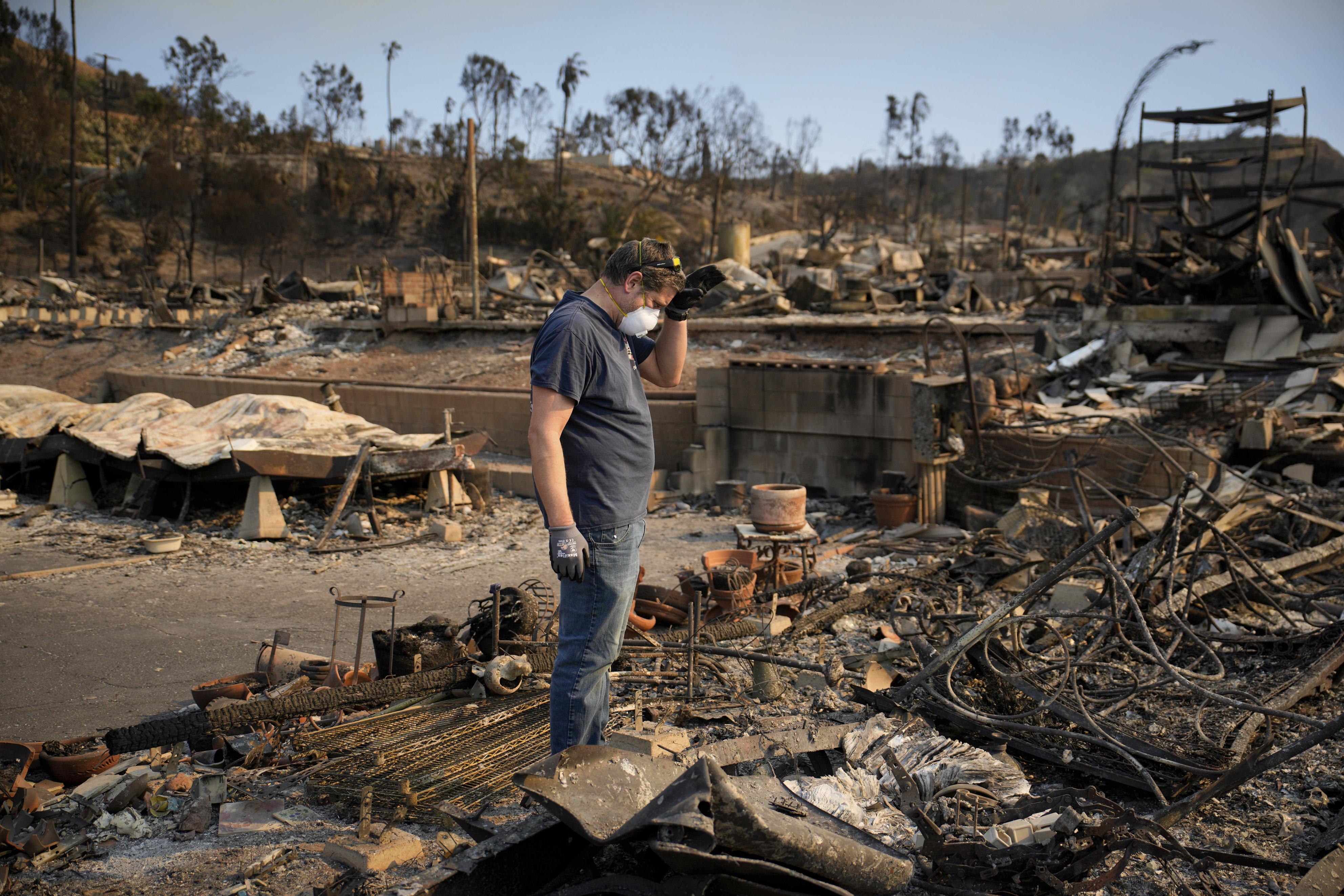 11日、米ロサンゼルスで、山火事で燃えた物件の状況を調べる男性（AP＝共同）