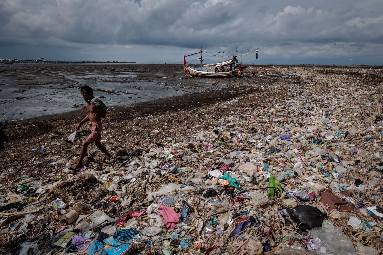 A man walks on a beach filled with plastic waste at Muncar port.
