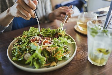 a close up of a person eating a leafy green salad with a side of water with lemon, to help them reach 2,000 calories per day.