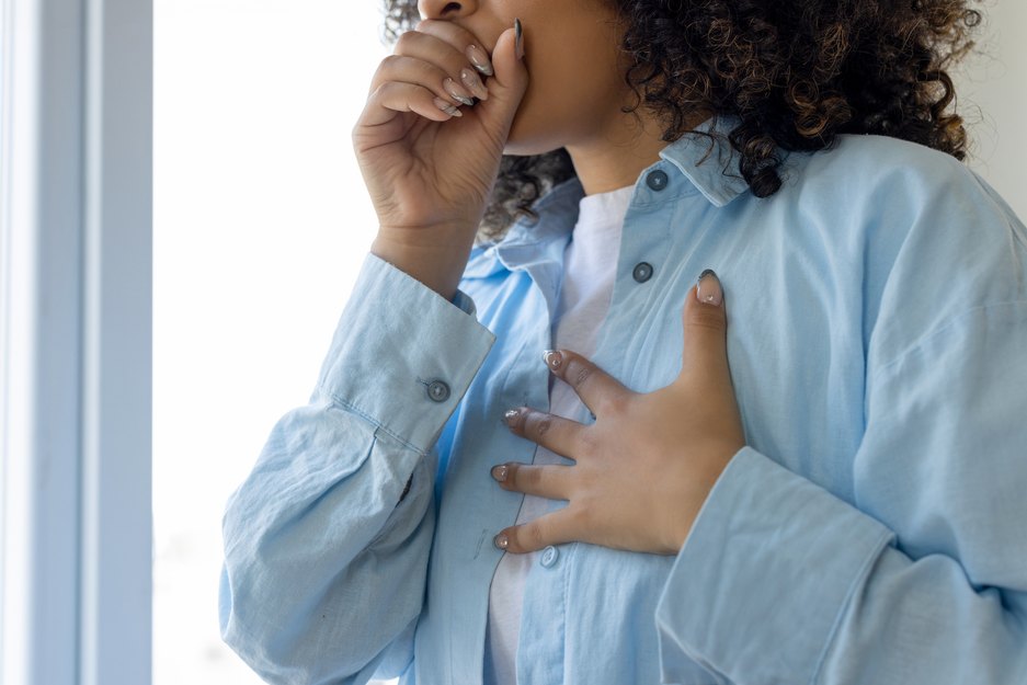 woman holding her chest while coughing into her hand