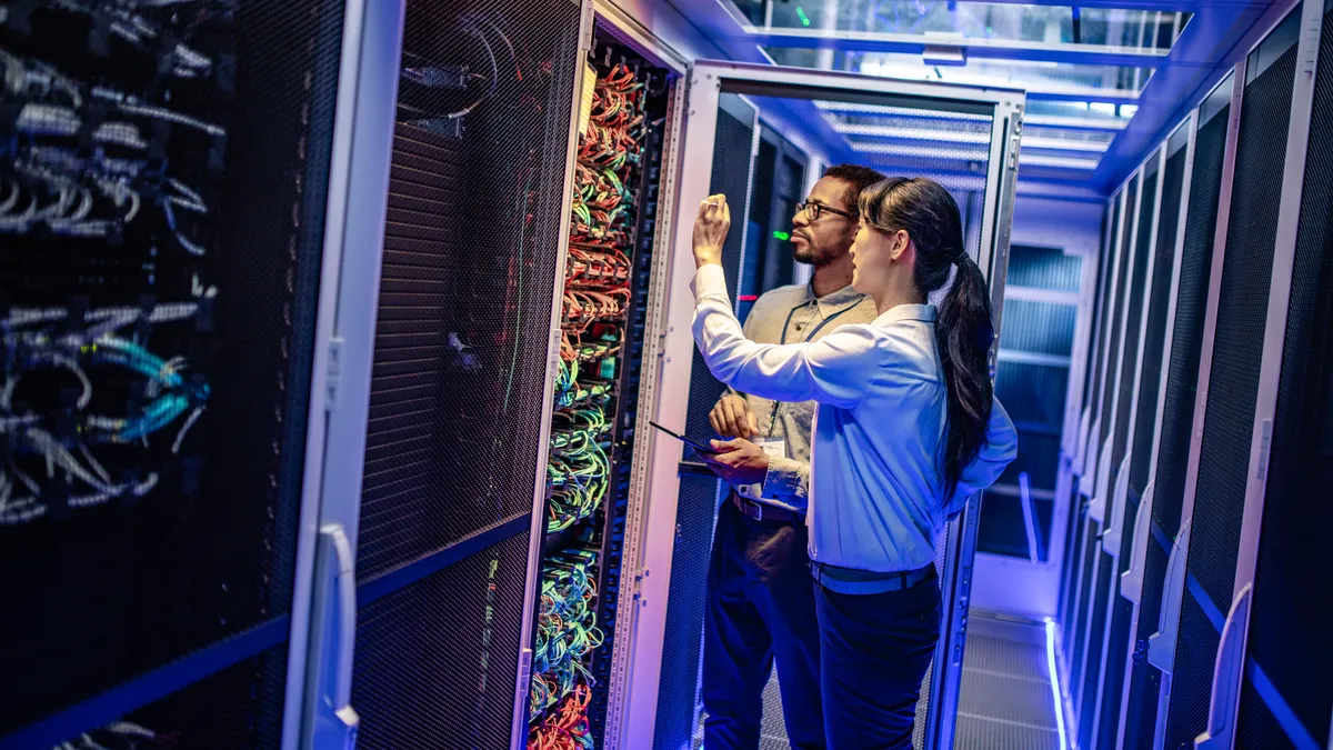 Two technology workers stand in front of a large server unit