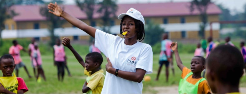 Photo d'une personne représentant l'association Play International qui arbitre un jeu entre des équipes d'enfants.