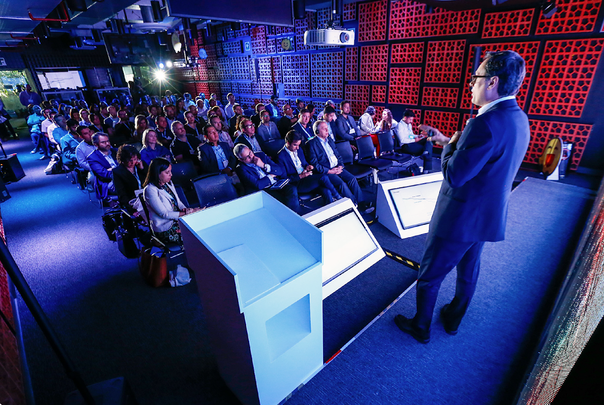 A man on stage speaking to a full audience at a conference.