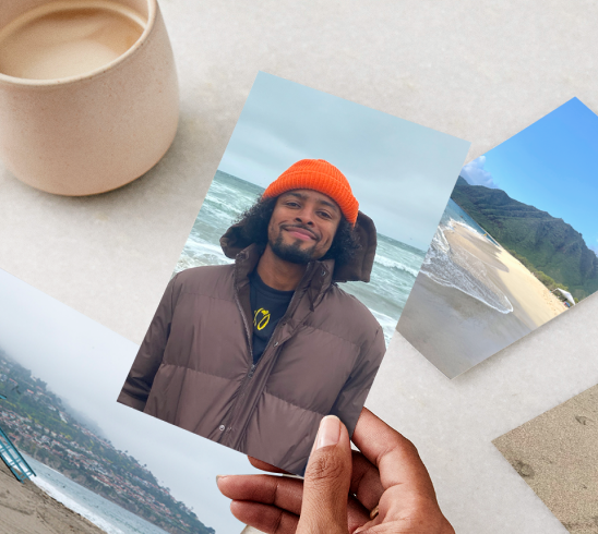 A hand holding a photo print of a man in jacket and orange winter hat.