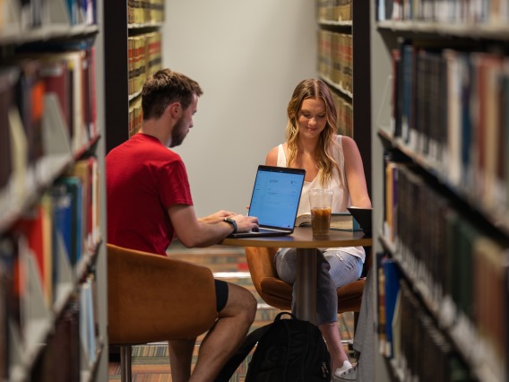 two students studying in book stacks