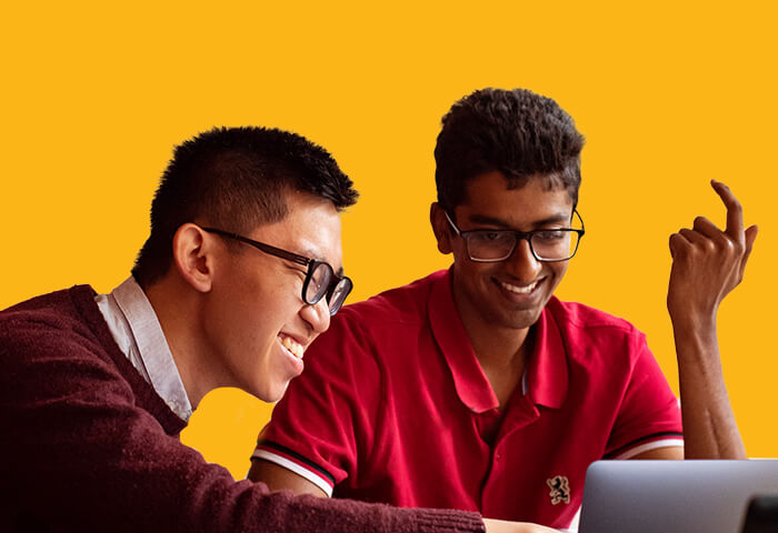 Two young people smiling while looking at a computer screen.