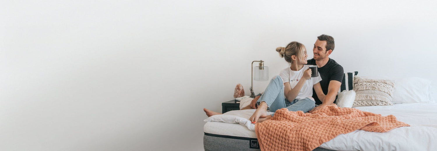 A happy couple sitting on a lull mattress with a cup of coffee.