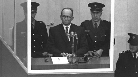 JERUSALEM, ISRAEL: (FILE PHOTO) Nazi war criminal Adolph Eichmann stands in a protective glass booth flanked by Israeli police during his trial April 5, 1961 in Jerusalem. The Israeli police donated Eichmann&apos;s original handprints, fingerprints and mugshot to Jerusalem&apos;s Yad Vashem Holocaust memorial ahead of Israel&apos;s annual Holocaust remembrance day May 4, 2005 which this year also marks the 60th anniversary of the Nazi&apos;s World War II defeat in 1945. (Photo by GPO via Getty Images)