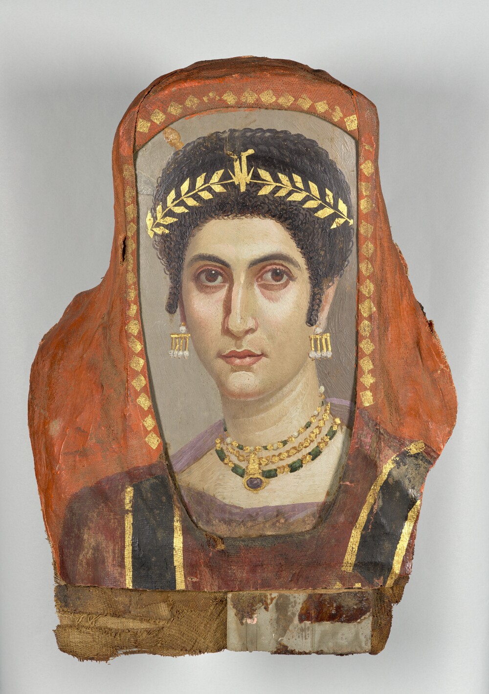 An ancient portrait in gold and colorful wax of a woman with large eyes and dark brown hair, adorned with earrings, a diadem, and bejeweled necklaces