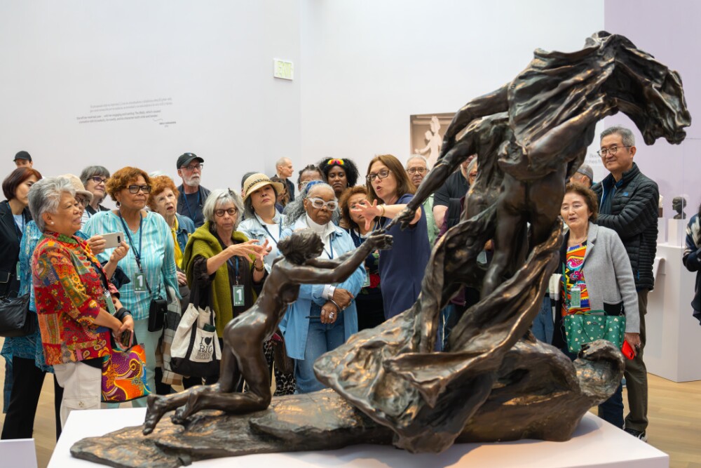 A group of people look at sculptures behind glass displays in an art gallery with high walls and lots of natural light