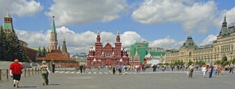 Panoramisk foto af Den Røde Plads i Moskva. Blå himmel med hvide skyer over det rødbrune Lenin-mausoleum, til højre herfor ses stilladser beklædt med grønt.