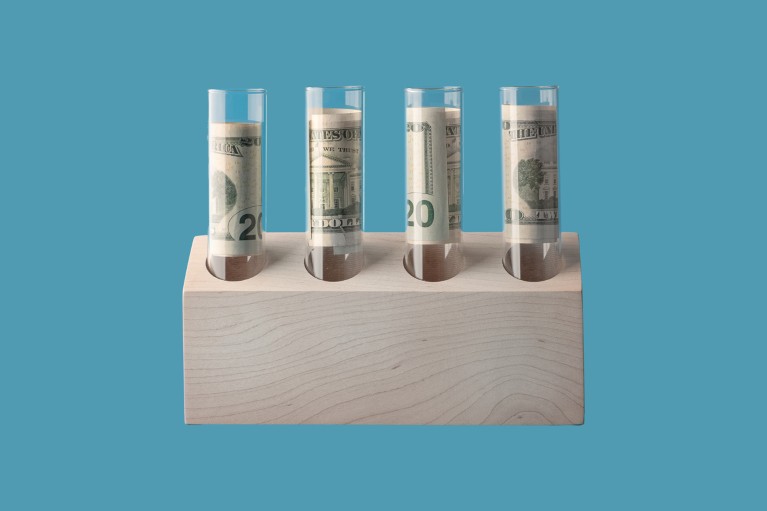 Four glass test tubes in a test tube holder with rolled up US bank notes inside