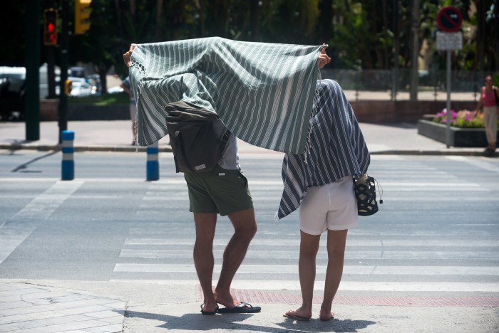 Two people cover themselves with stripy towels to protect themselves from the sun