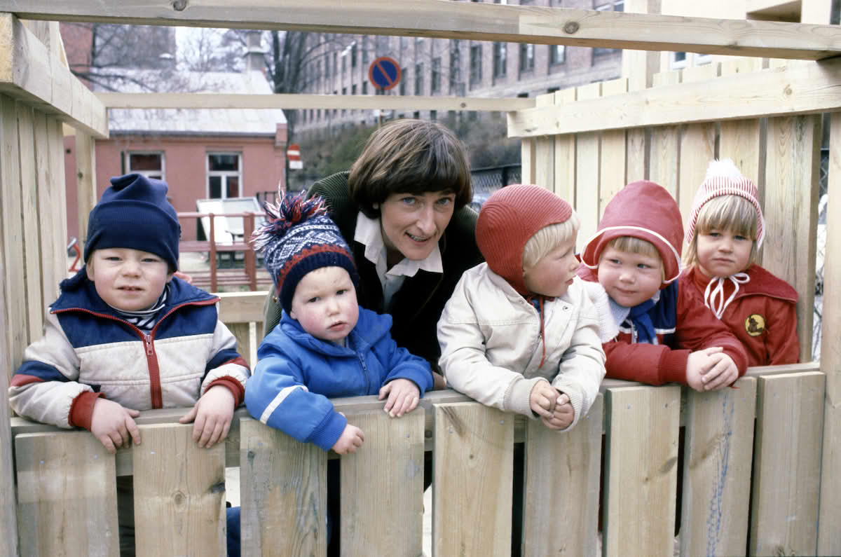 Foto av Rønbeck sammen med fem små barn. Alle står innenfor et plankegjerde i en barnehage.