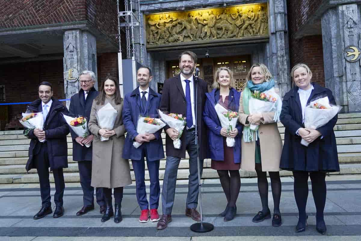 Bilde av det nye byrådet foran inngangsdøra til Rådhuset. Alle smiler og holder en blomsterbukett foran seg. 