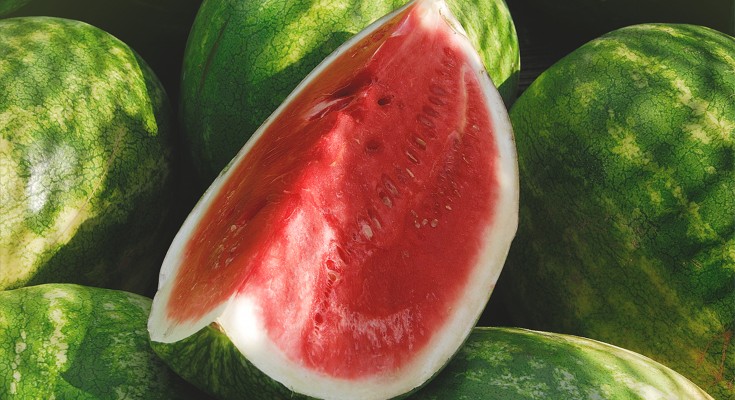 Shaded cut watermelon on top of other watermelons