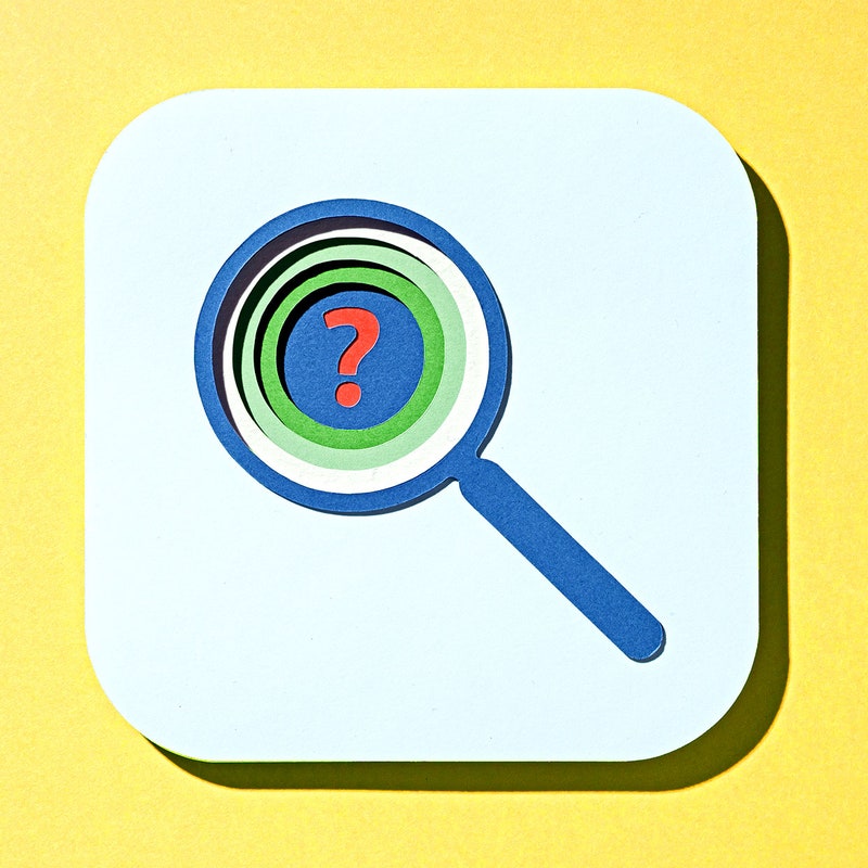 Multi layered paper cut outs of a blue and green magnifying glass with a red question mark in the center on a yellow background