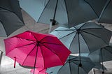 Many gray umbrellas with one red umbrella