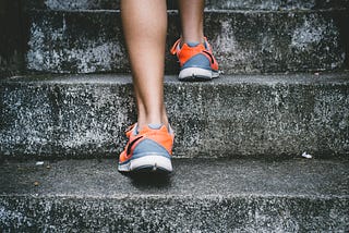 pair of legs wearing shoes taking steps up concrete stairs