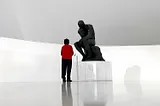 A woman looking at a statue of the thinker in a futuristic art gallery.