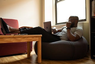 Man working on a beanbag with his legs up on a desk.