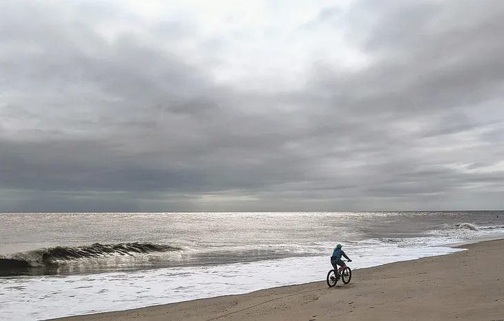 A silhouette of a lone biker pedaling along a beach.