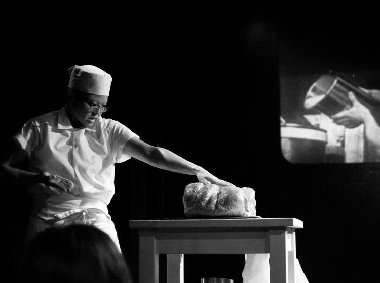 A black and white image of a man standing by a table