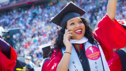 A jubilant graduate with a sticker reading "First Generation Student" on her graduation gown