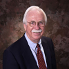 Jack Davis facing forward, white hair and mustache, wearing a dark suit, white shirt and maroon tie