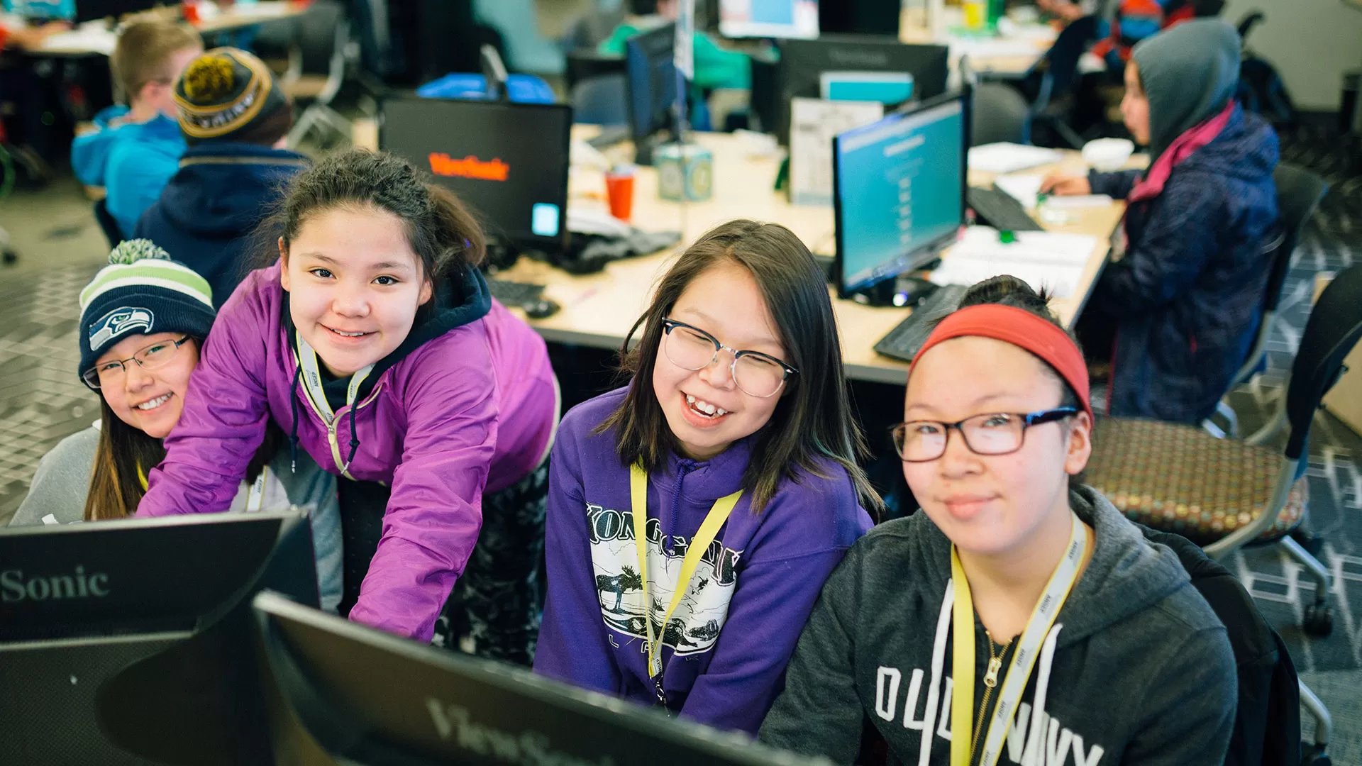 Four smiling kids behind computers.