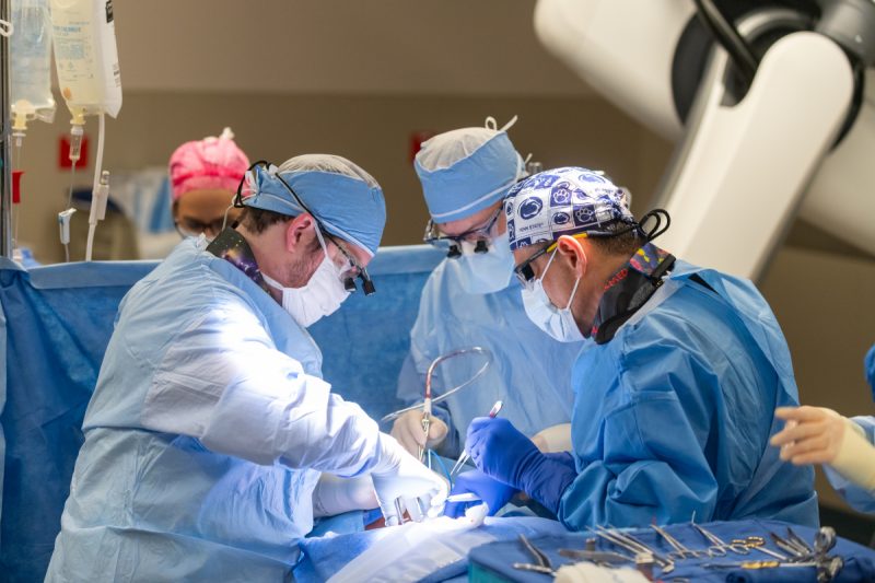 Two doctors perform a transcarotid artery revascularization procedure at Penn State Health St. Joseph Medical Center. They are focused and working in a well-lit operating room, using medical instruments and equipment to carry out the procedure.