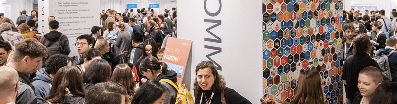 Large group of people in a conference space around columns with 'Community' text graphics and a tessellation of hex stickers