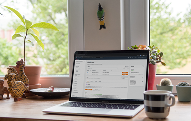 A desk scene by a window with a laptop logged into AWS, a coffee cup, and some potted plants.