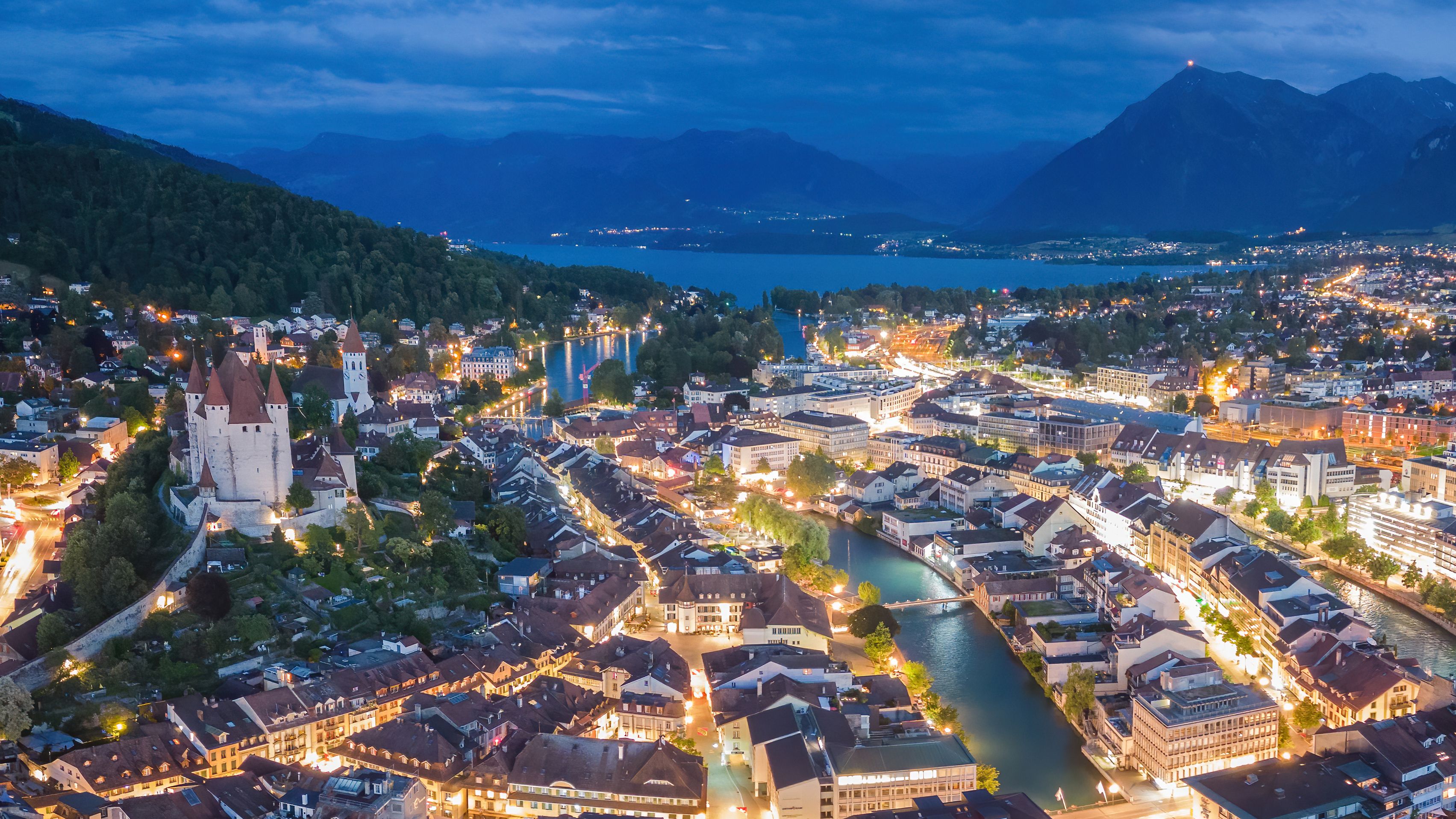 Luftaufnahme der Thuner Altstadt bei Nacht, im Hintergrund der Thunersee und die Berner Alpen.