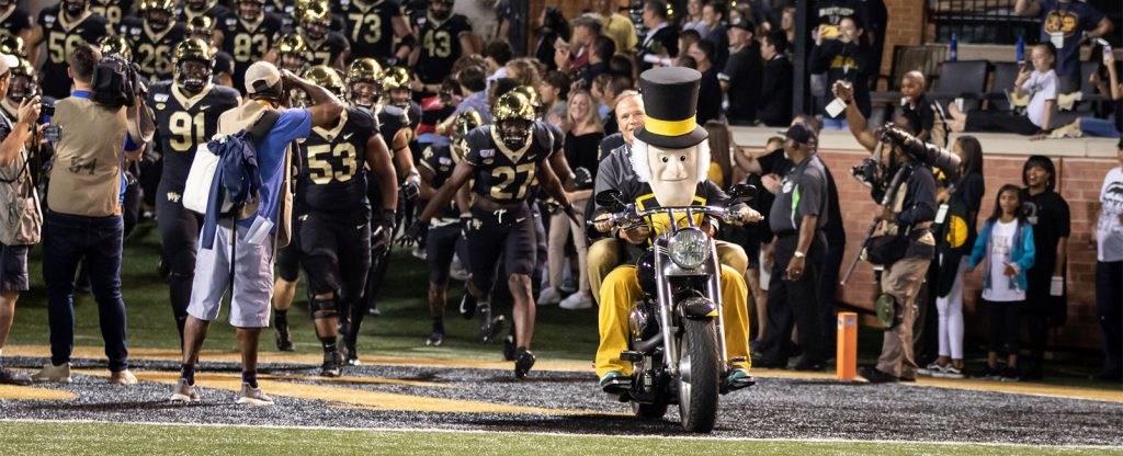 Demon Deacon rides his motorcycle during a football game.