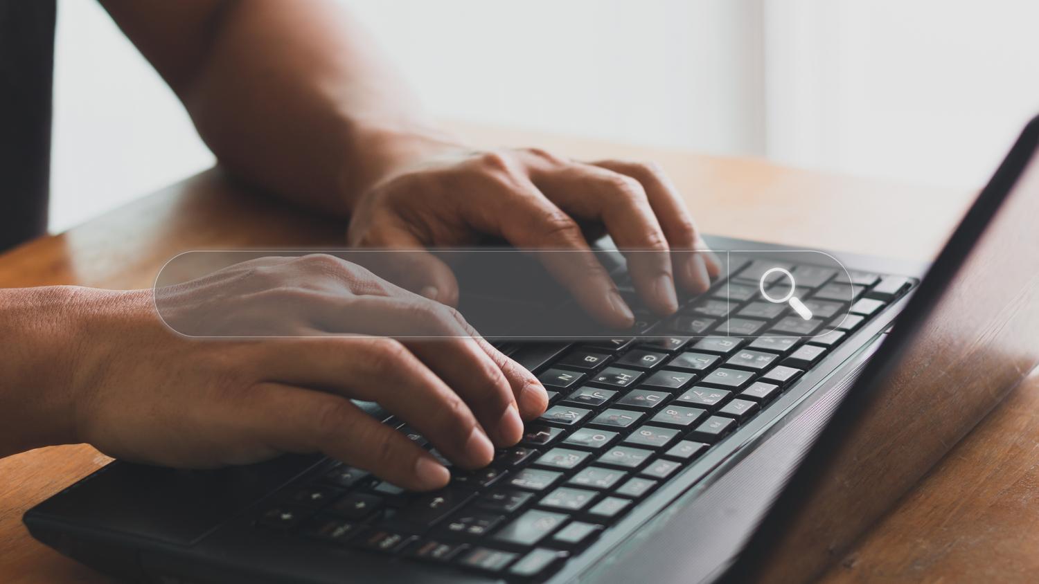 Hands typing on a laptop keyboard with a search bar superimposed over it