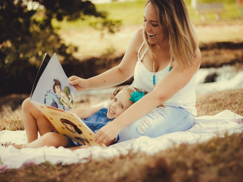 woman reading to a small child on a blanket