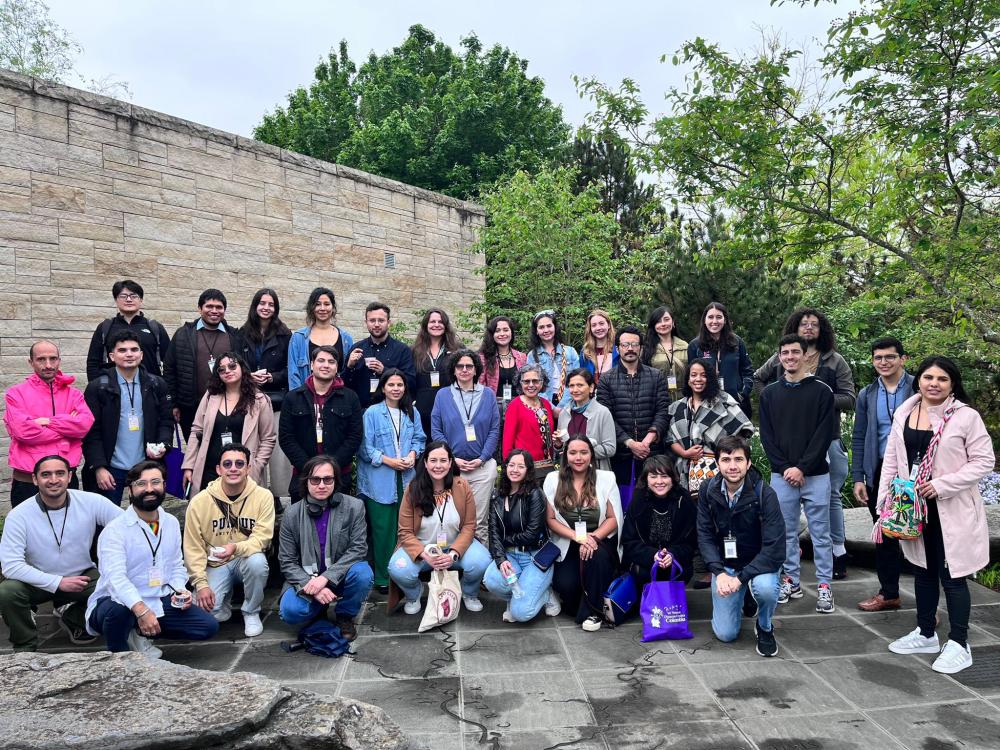 A large group of people smiling for a picture outside next to a wall