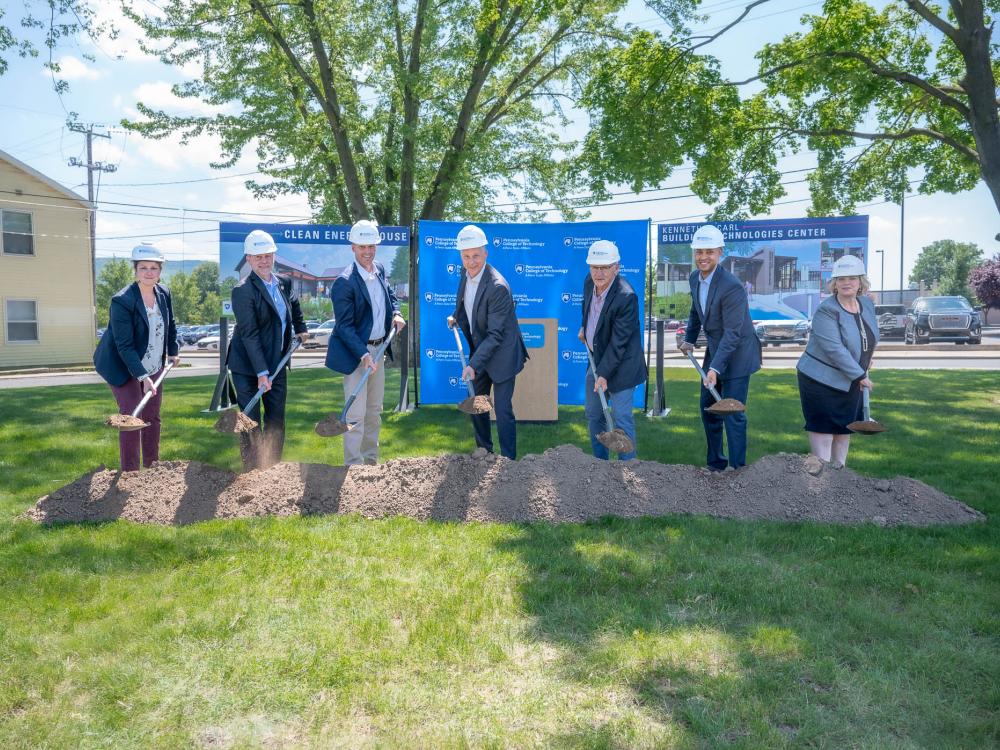A line of people wearing hard hats use shovels to break ground for construction